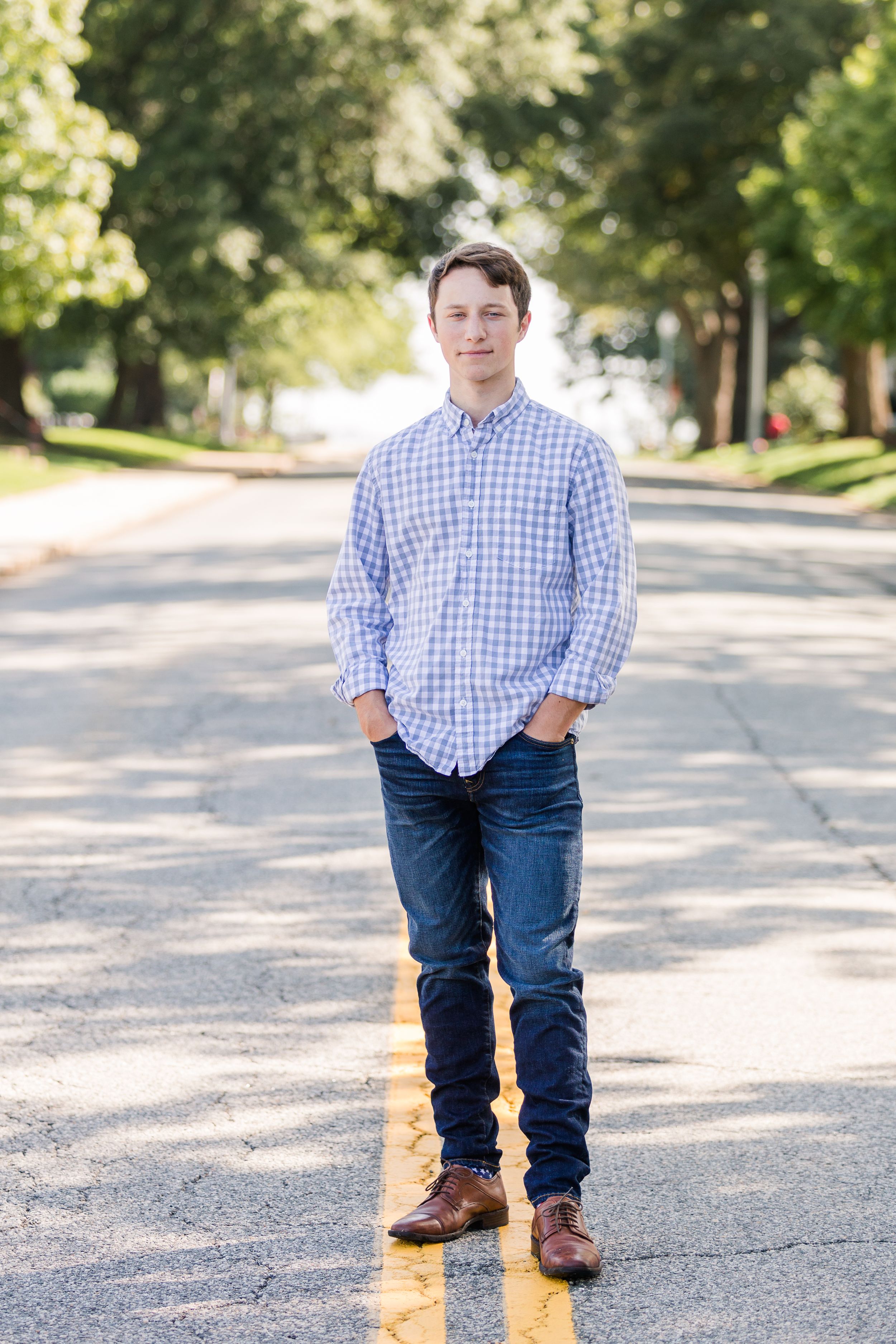 Senior boy standing with hands in pockets on tree lined street