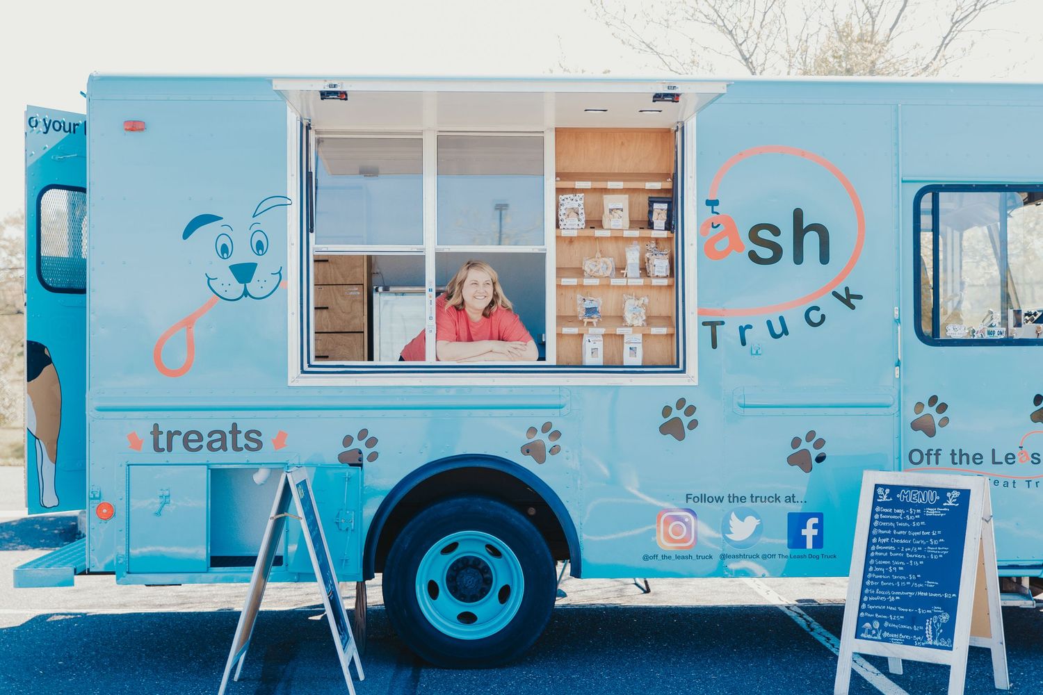 Blue and white food truck with paw print designs serving treats in a parking lot.