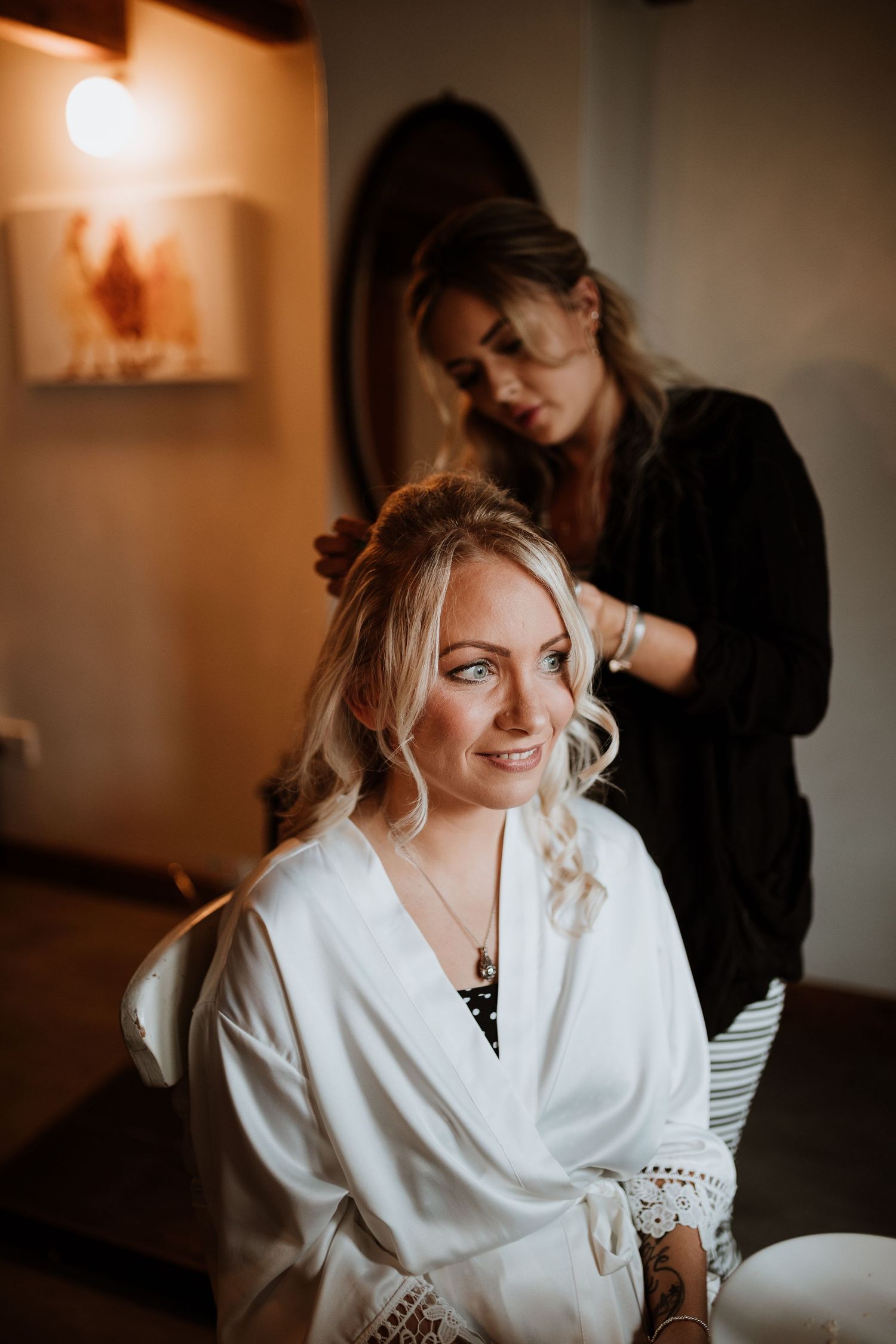 brides hair being done before wedding whilst bride watches guests out of window