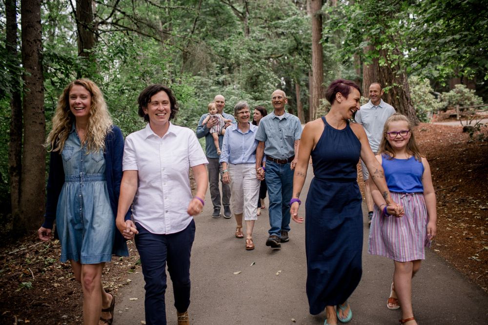 Extended family group walking together on shaded forest path during outdoor summer photo session.