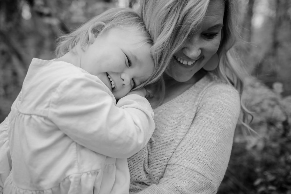 Black and white photo of smiling mother and laughing toddler sharing a joyful embrace outdoors.