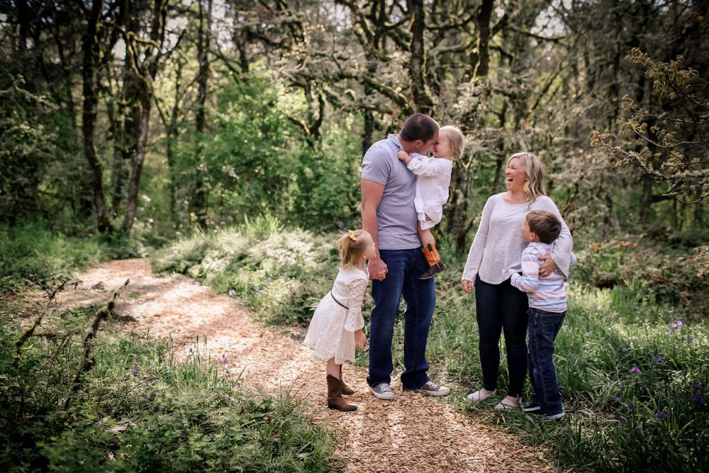 Family of five walking on sunlit forest trail, parents with three young children in nature.