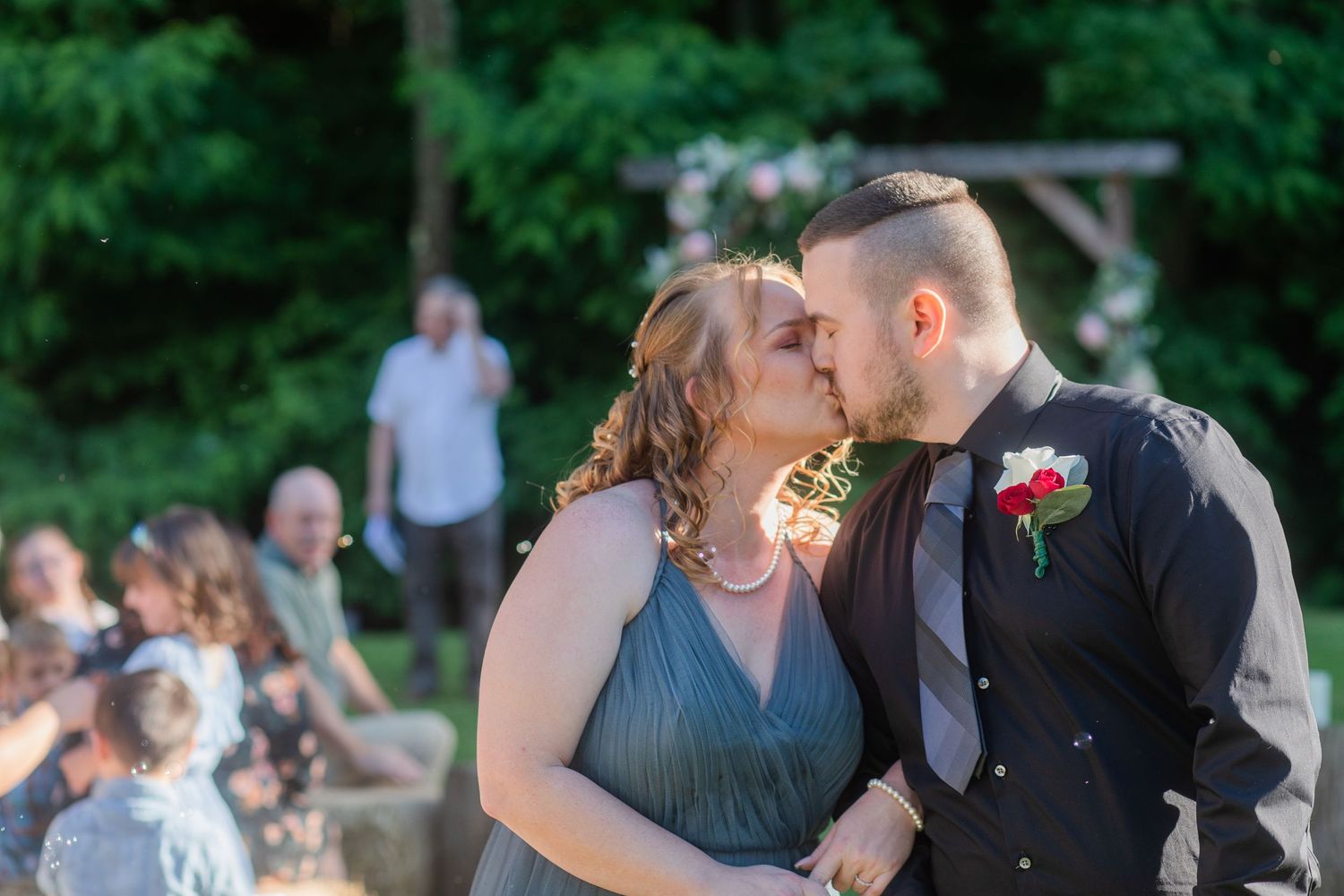 Romantic outdoor wedding ceremony moment under a flower-decorated wooden arbor.