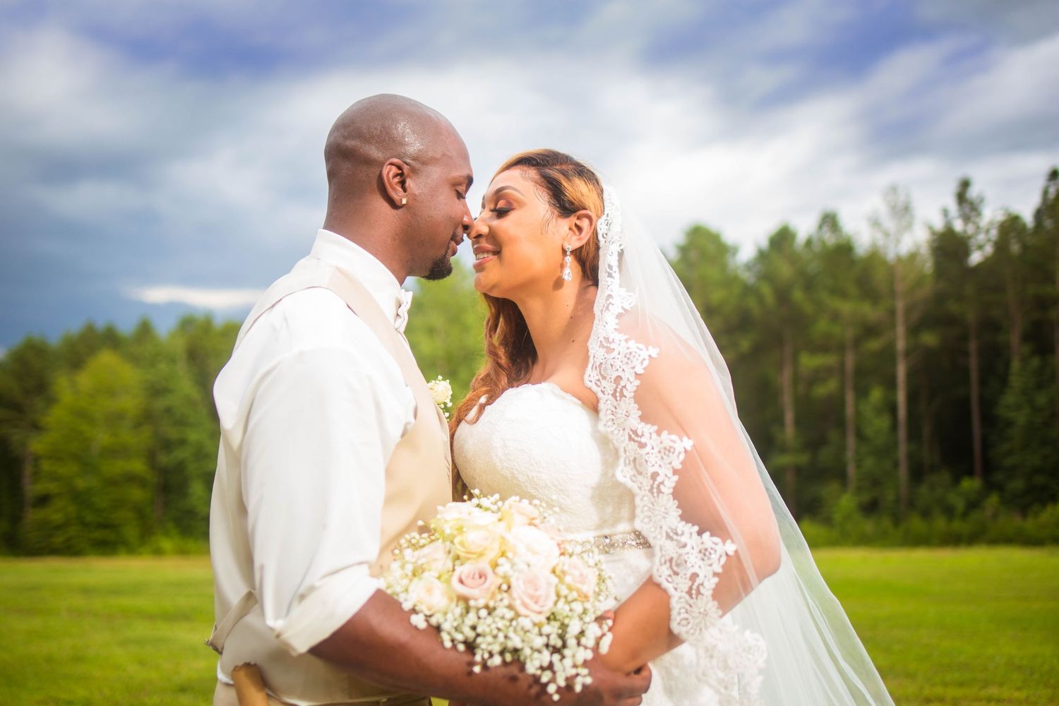 Newlywed couple embraces in romantic outdoor wedding photos with lush greenery in the background.