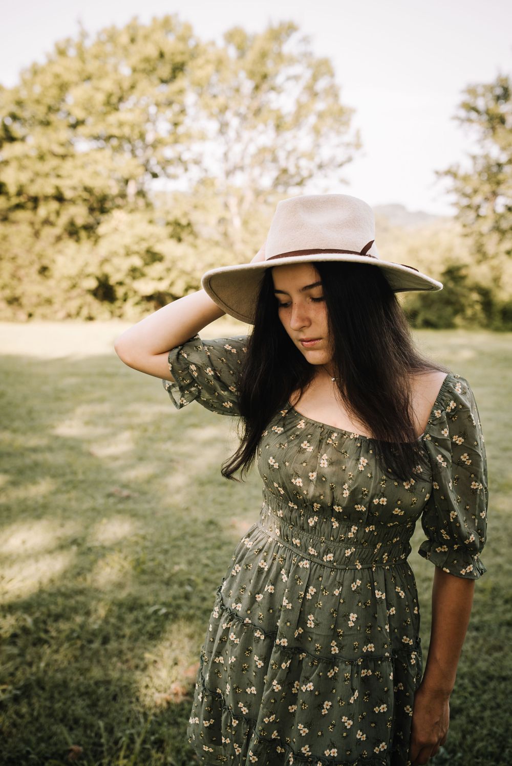 Someone in a floral dress and wide-brim hat poses in a sunny garden setting.