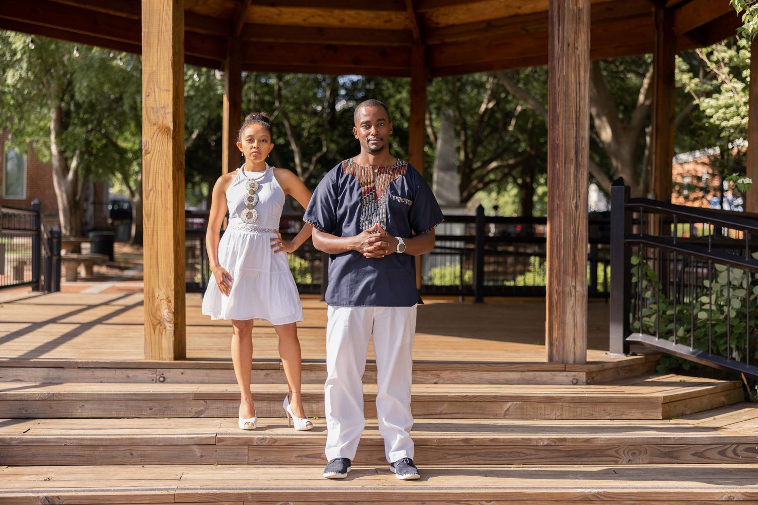 A couple standing in a wooden gazebo surrounded by lush green trees and natural lighting.