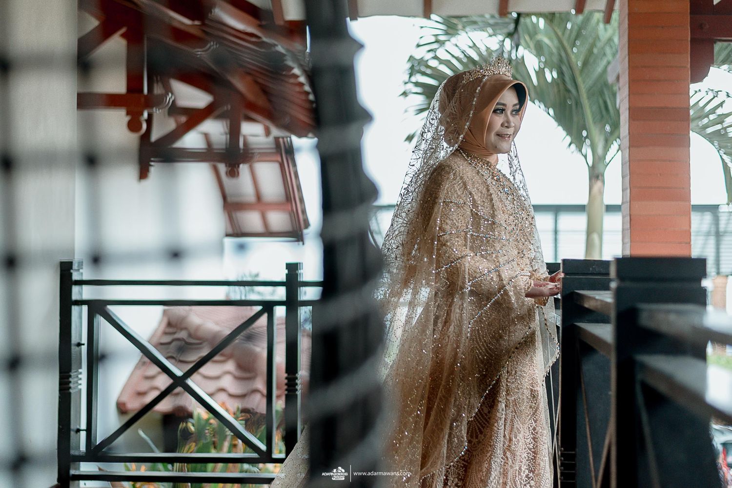 Elegant bride in sparkly champagne gown poses gracefully on a balcony during her wedding photoshoot.