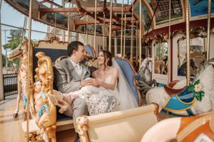 Newlyweds share intimate moment on vintage carousel with decorative horses.