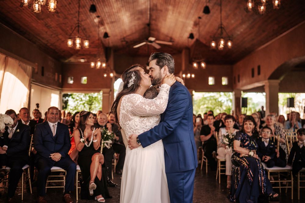 Wedding couple shares first dance in elegant reception hall with warm lighting and applauding guests.