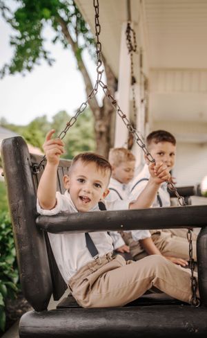 Young children in white shirts enjoying a vintage porch swing on a summer day.