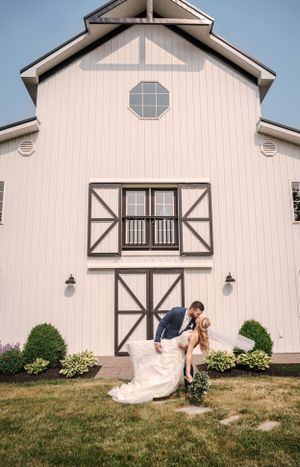 Romantic wedding pose in front of white barn-style building with black trim.