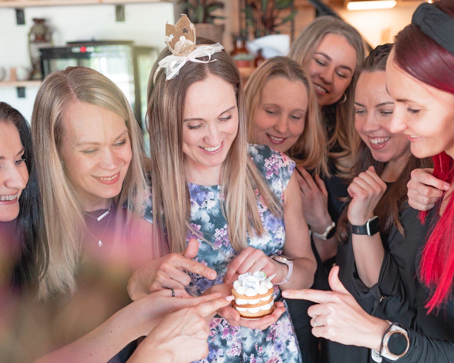 A group of friends gather excitedly around a cupcake at a social gathering.