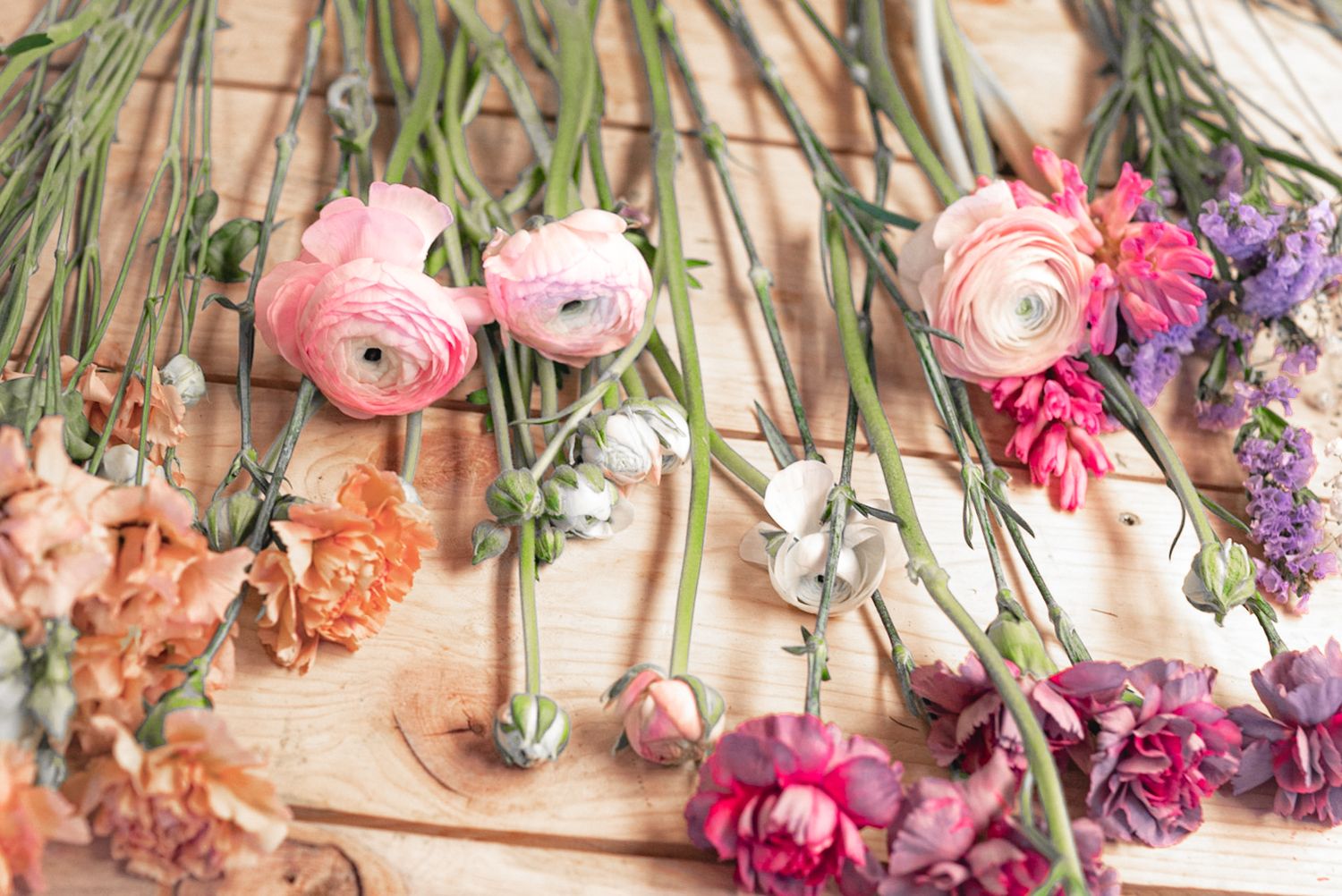 Fresh pink and purple flowers including ranunculus and carnations laid out on a wooden surface.