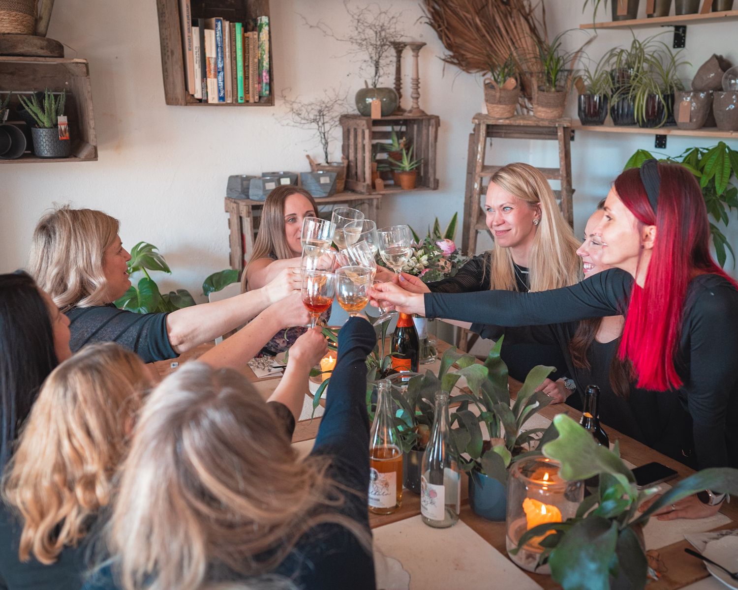 Friends toasting drinks together at a dinner party with rustic decor and greenery.