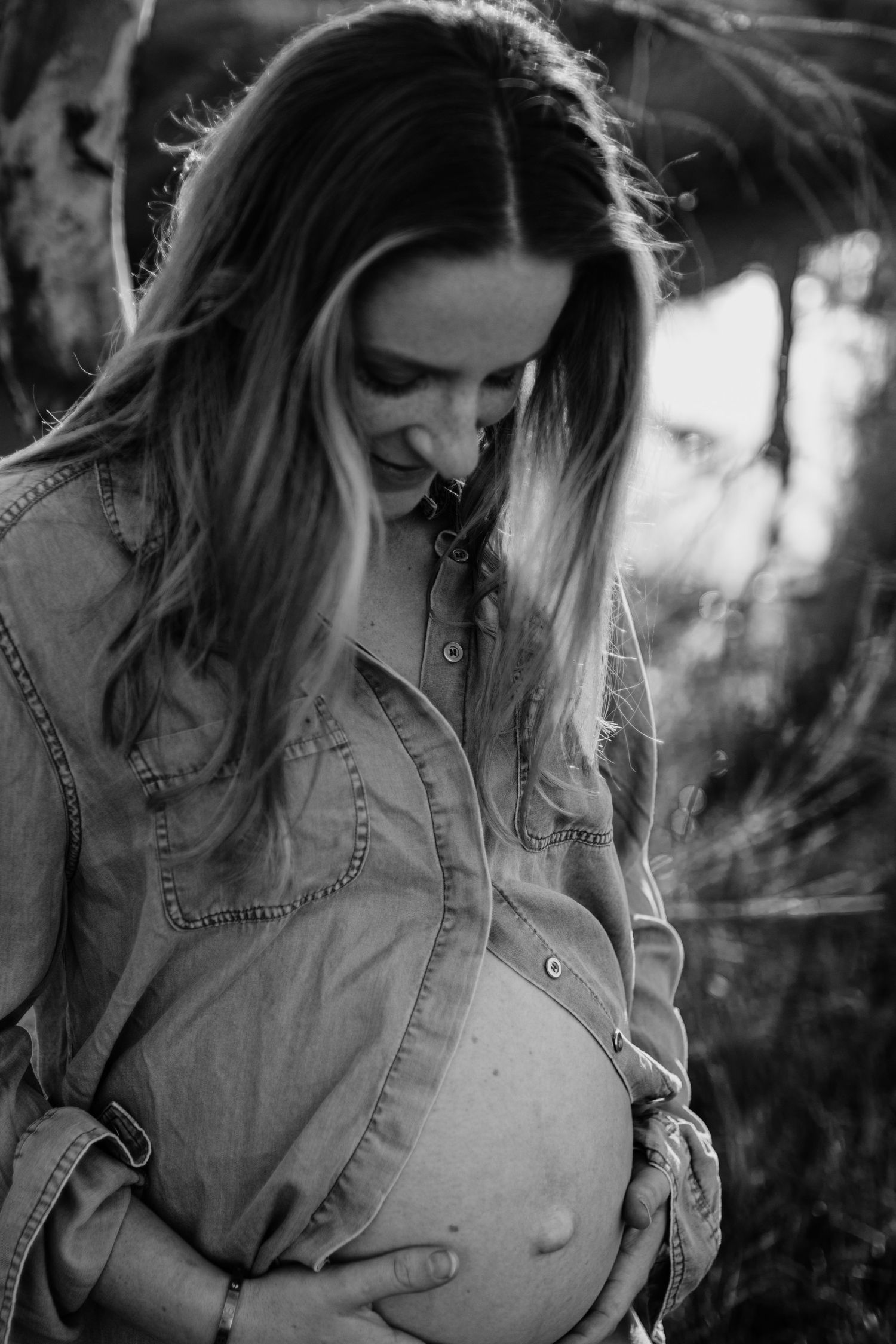 Black and white photograph of a pregnant mum looking down on her growing baby bump in a rural setting.