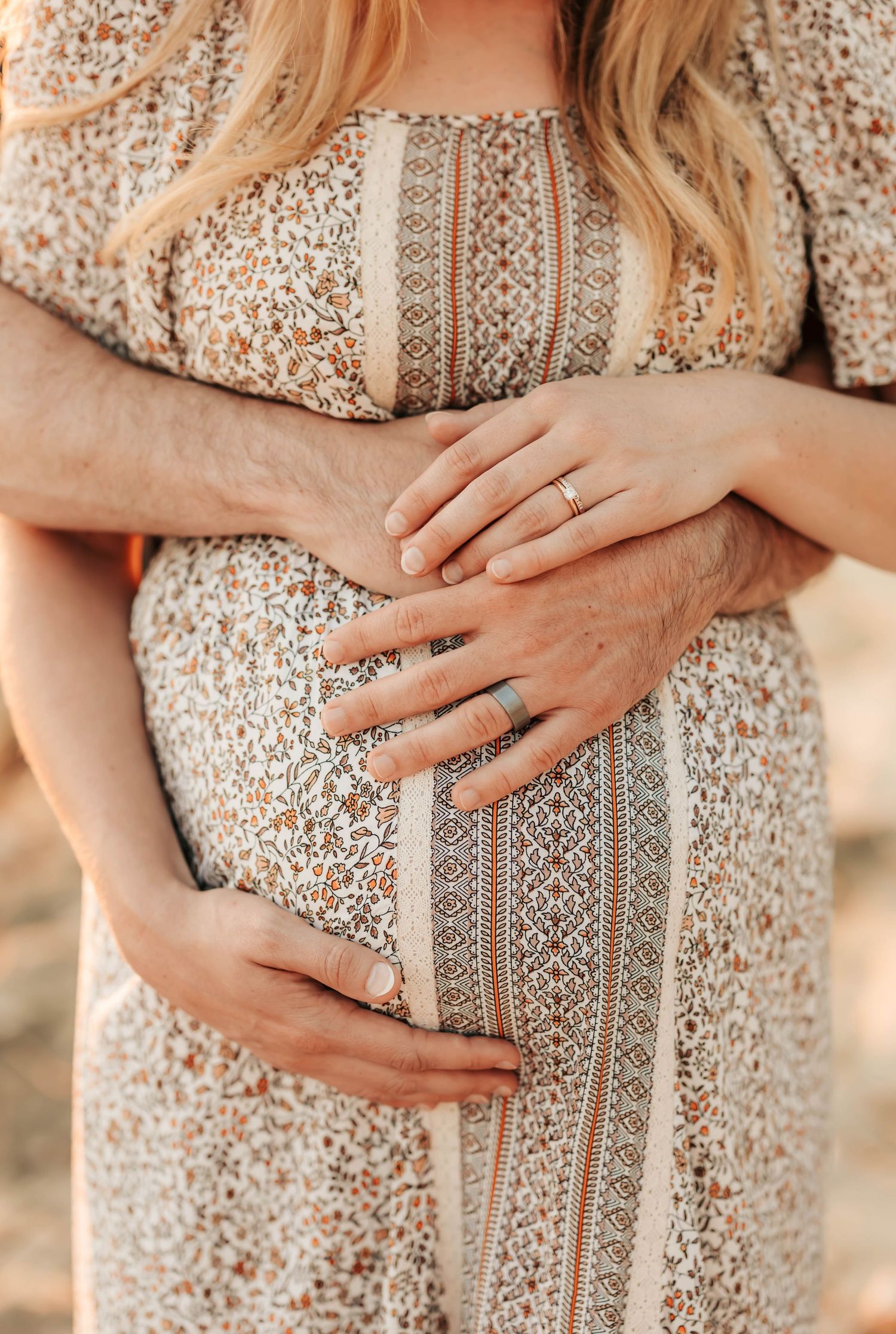 Close up of hands with engagement ring cradling a pregnant belly in a floral dress.
