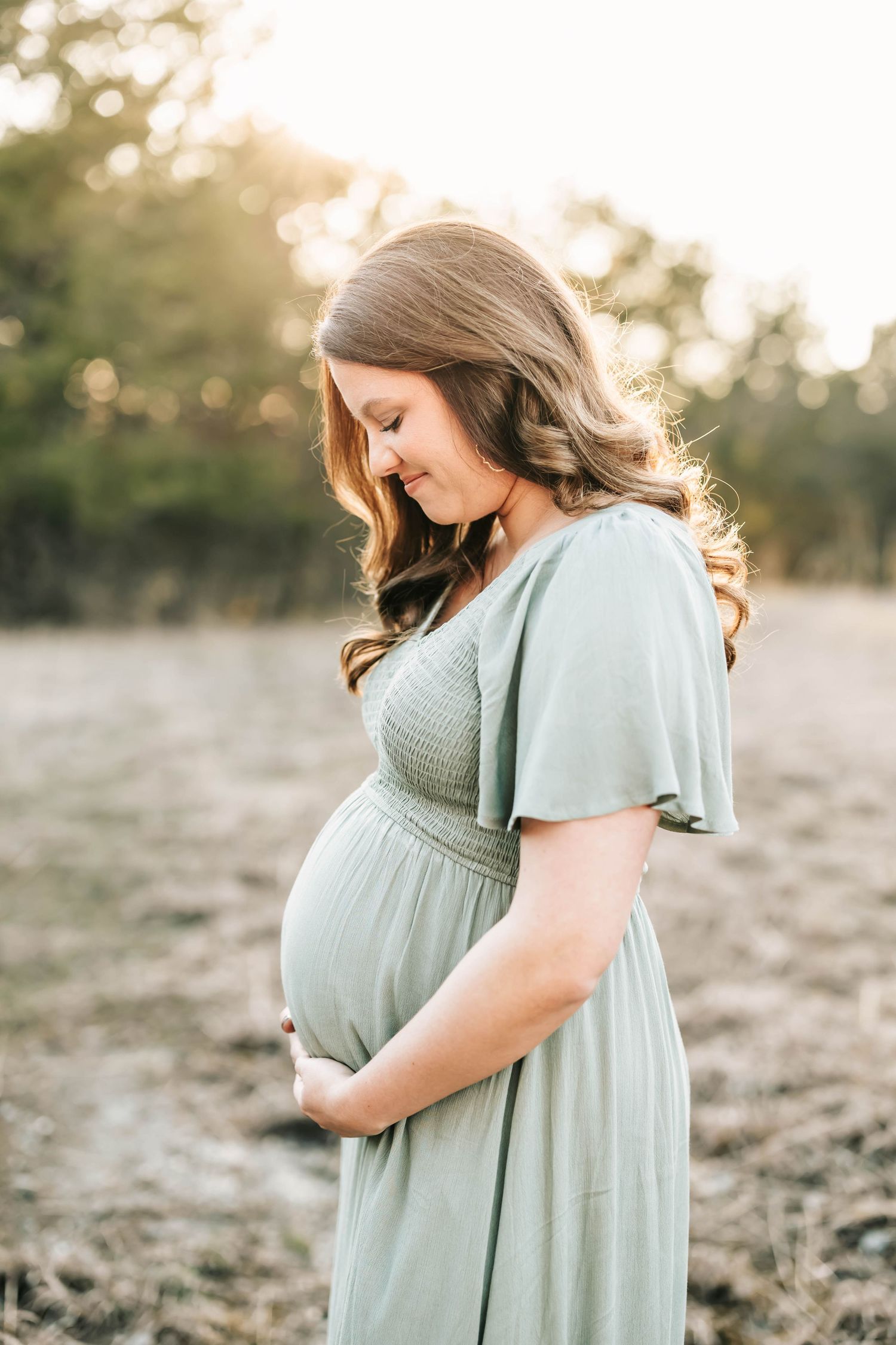 A serene maternity portrait of a woman in a sage green dress during golden hour.