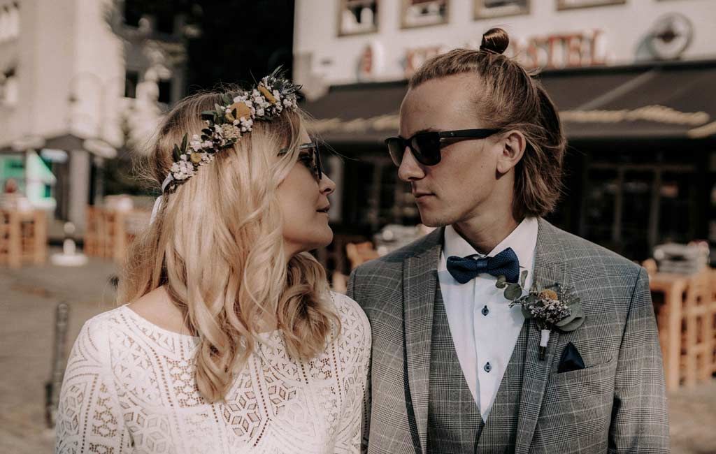 Stylish bride and groom in vintage-inspired attire pose together on city street.