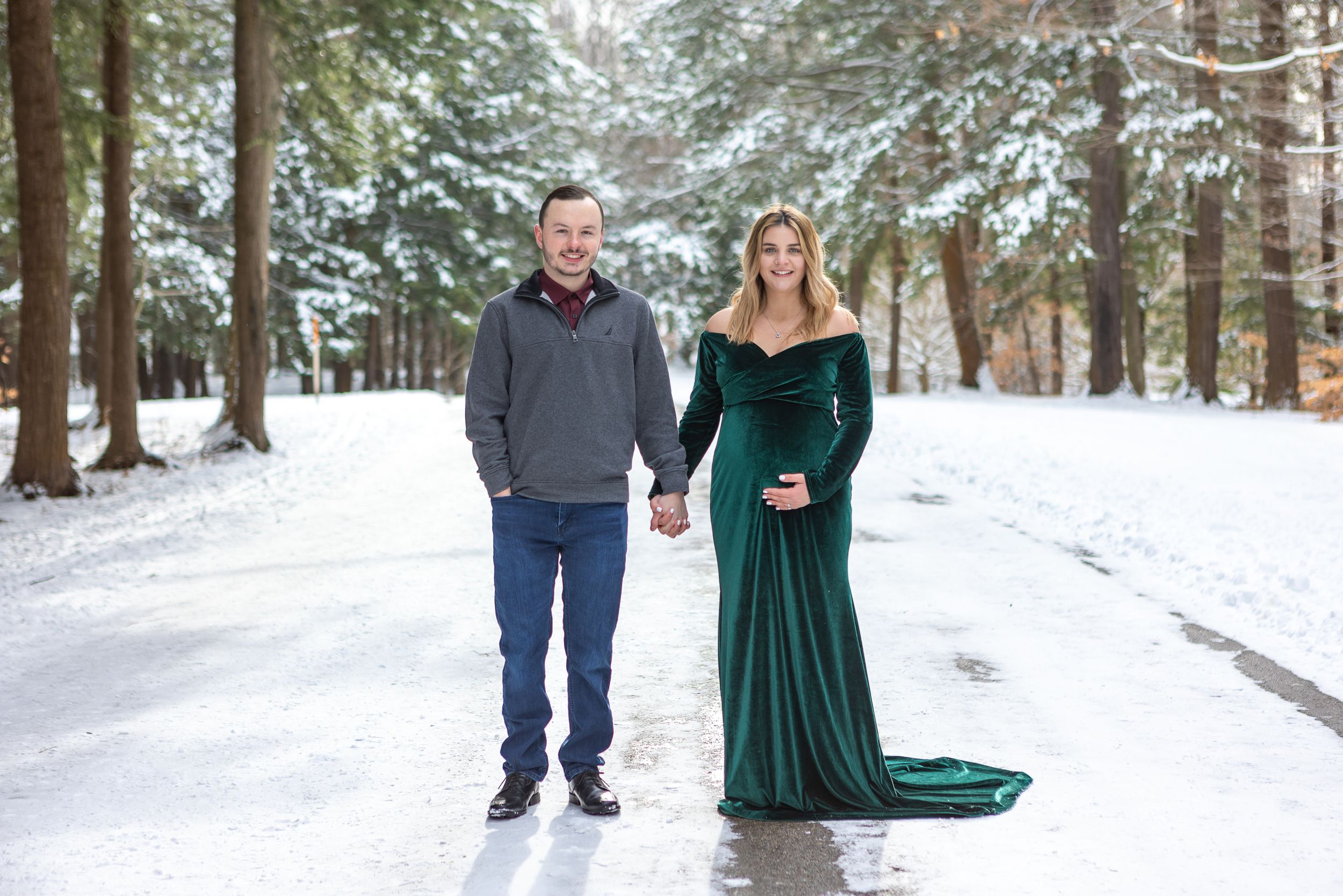 A winter maternity portrait with a flowing emerald dress contrasting against snow-covered trees.