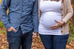 A couple holds hands while showing off a growing baby bump in casual fall attire.