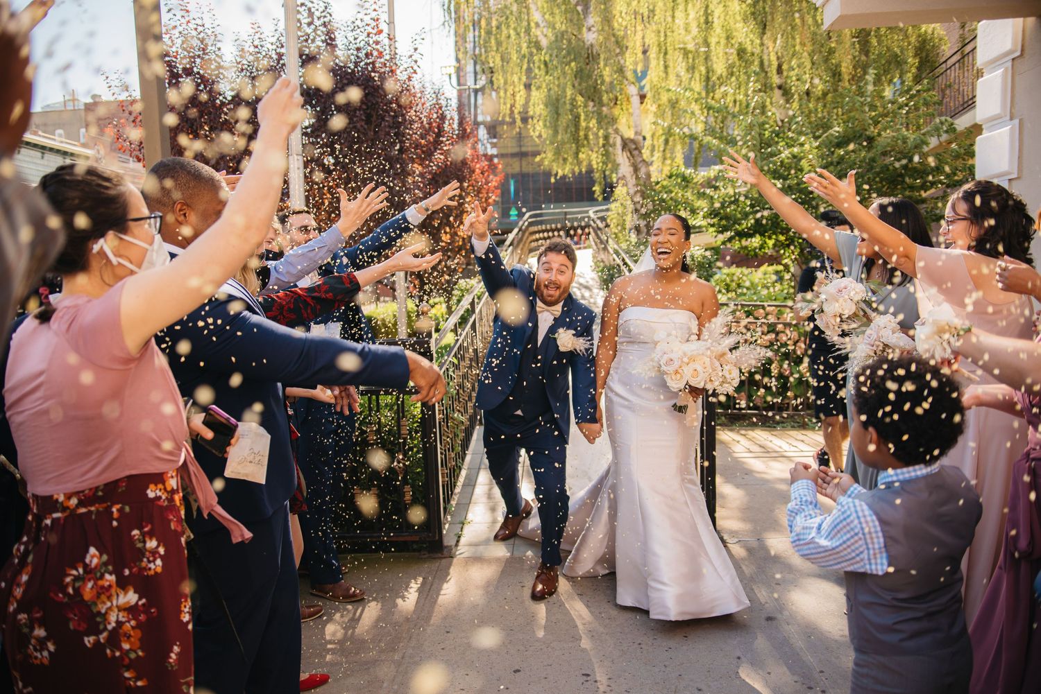 Wedding celebratory moment with confetti toss outside venue under willow trees.
