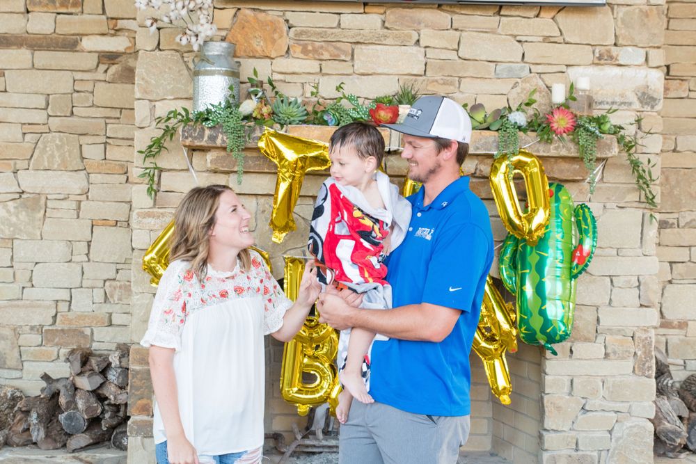 Outdoor celebration with festive gold and green balloon decorations against a stone wall background.