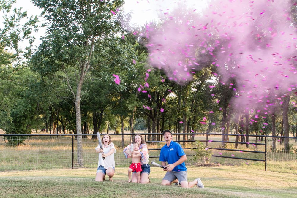 Pink smoke bomb gender reveal moment captured in an outdoor park setting.