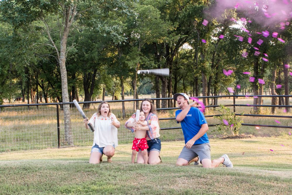 People celebrating in a park setting with pink smoke and trees in the background.
