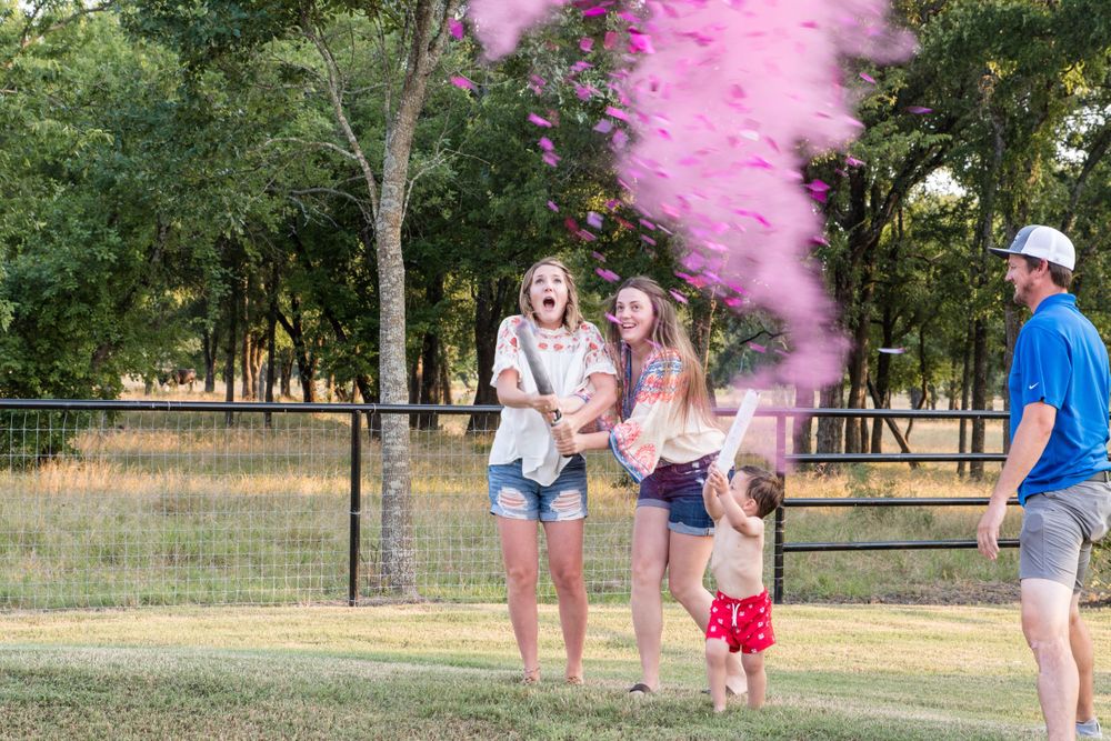 Pink smoke reveal celebration outdoors in a grassy field with fence and trees.