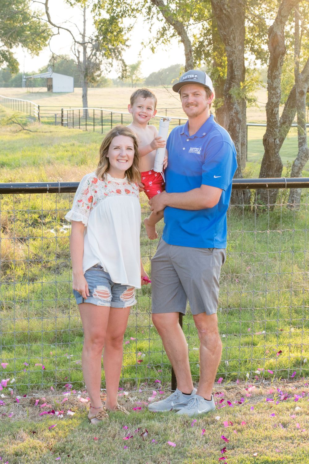 Family portrait in late afternoon sunlight with wooden fence and trees in background.