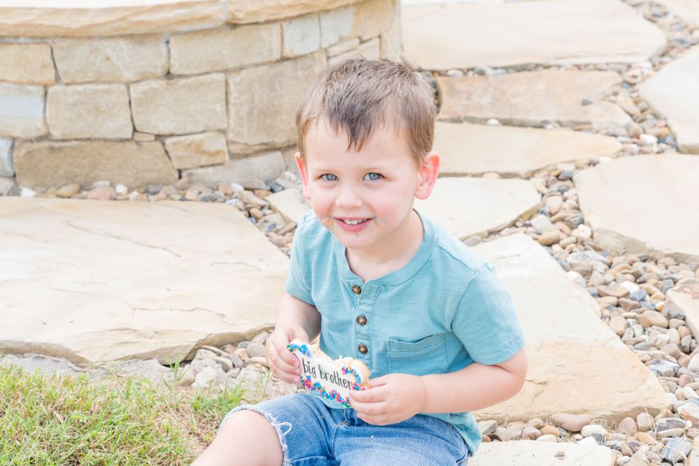 Young child in blue shirt sitting outdoors and enjoying party festivities.