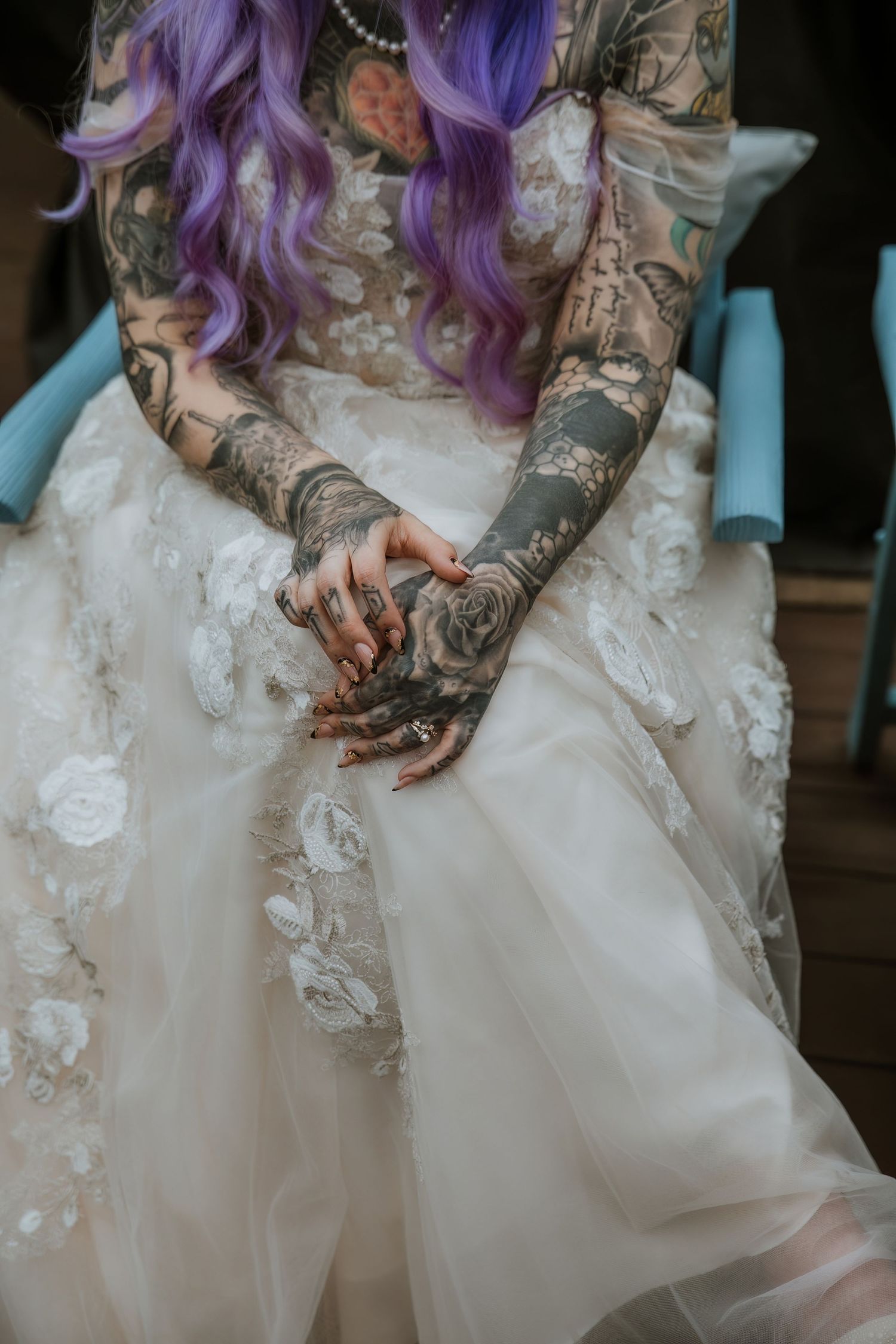 A closeup of a bride's tattooed hands folded on her lap in her wedding dress