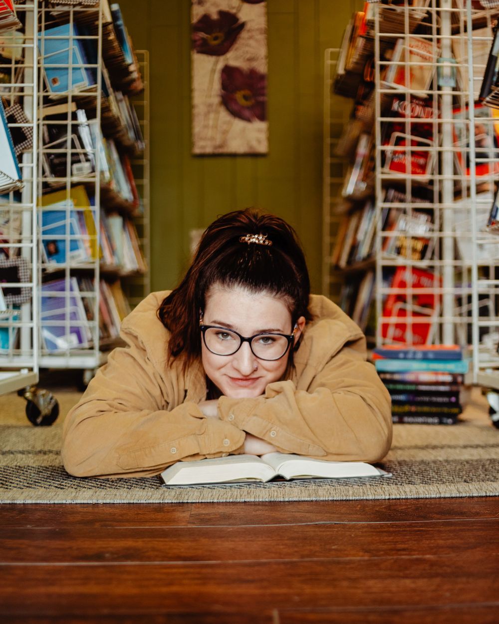 A bookstore scene showing someone resting their head on folded arms at a wooden counter with bookshelves behind.