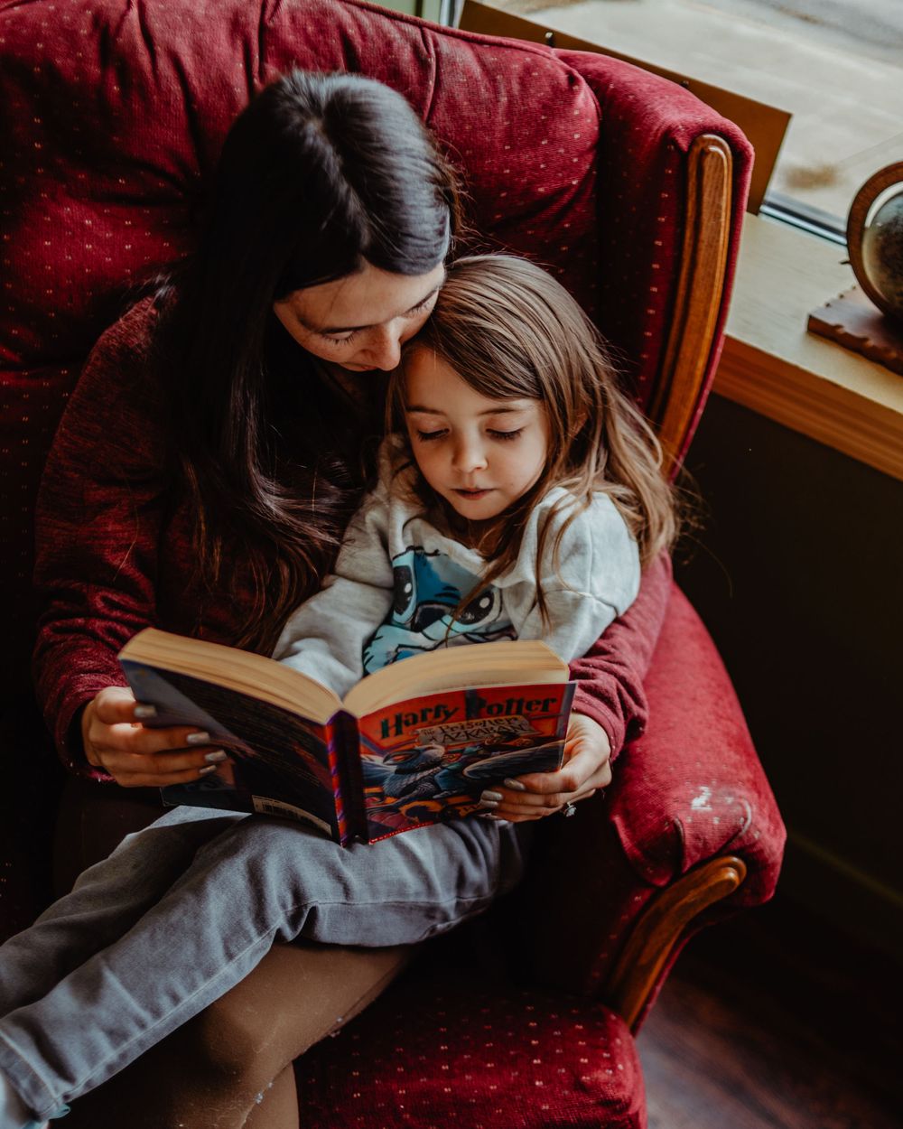 Intimate reading moment shared on plush red armchair with Harry Potter book.