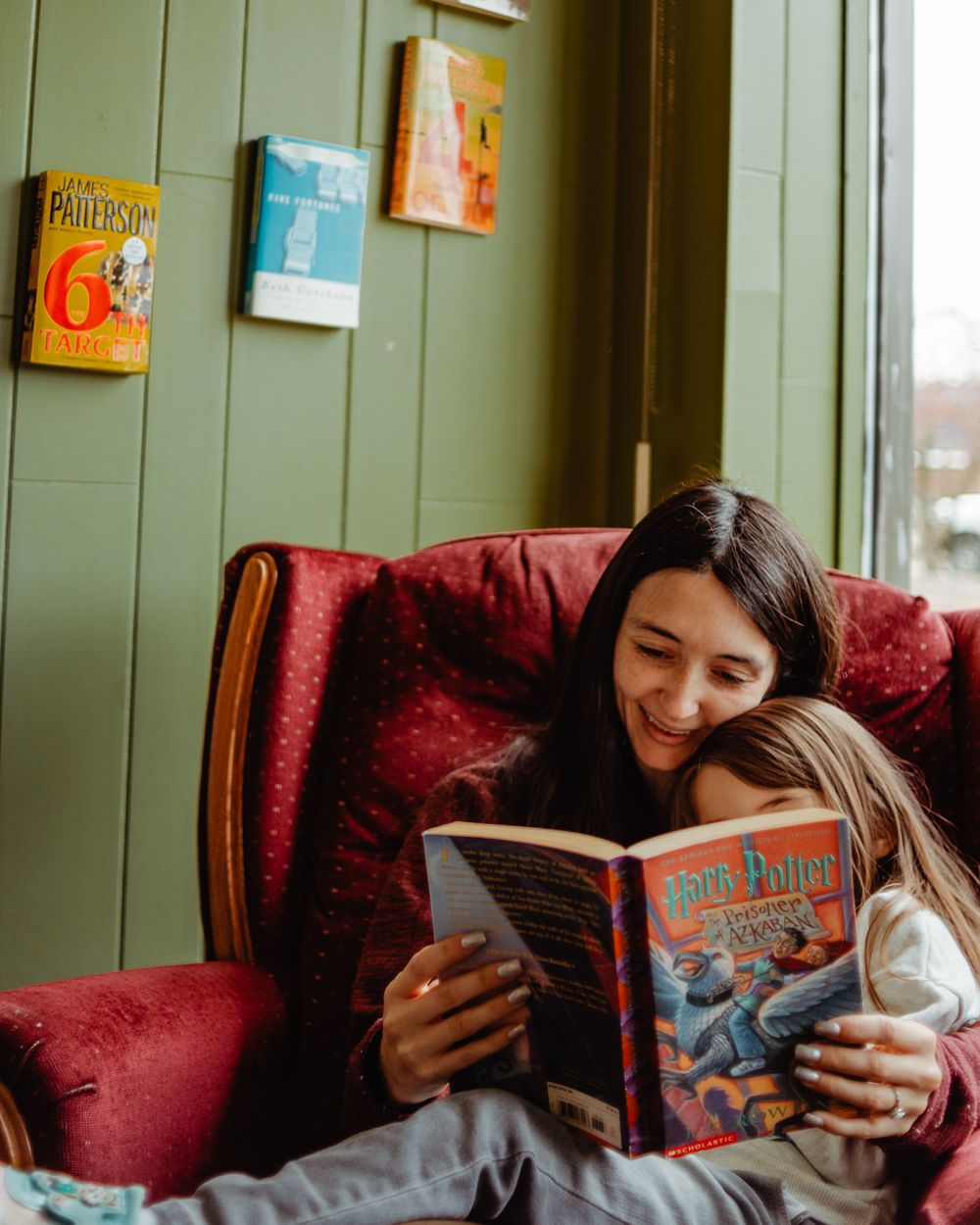 Cozy reading moment in red armchair with Harry Potter book against sage green wall.