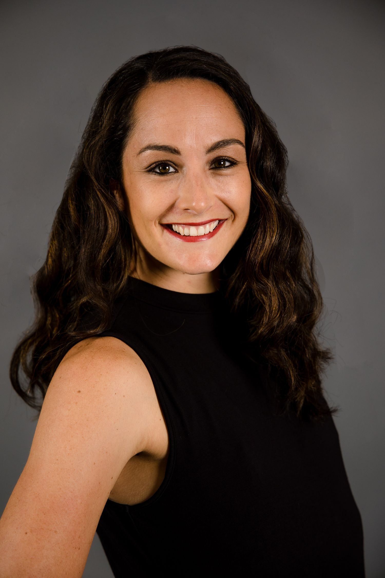 Studio portrait of a person in a sleeveless black top with wavy dark hair.