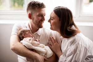 Family photo of mum, dad and newborn baby infront of a window in Beaminster, Dorset