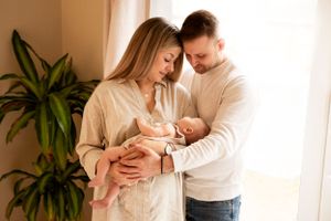 In-home family session with mother and father cuddling their newborn son infront of a big window