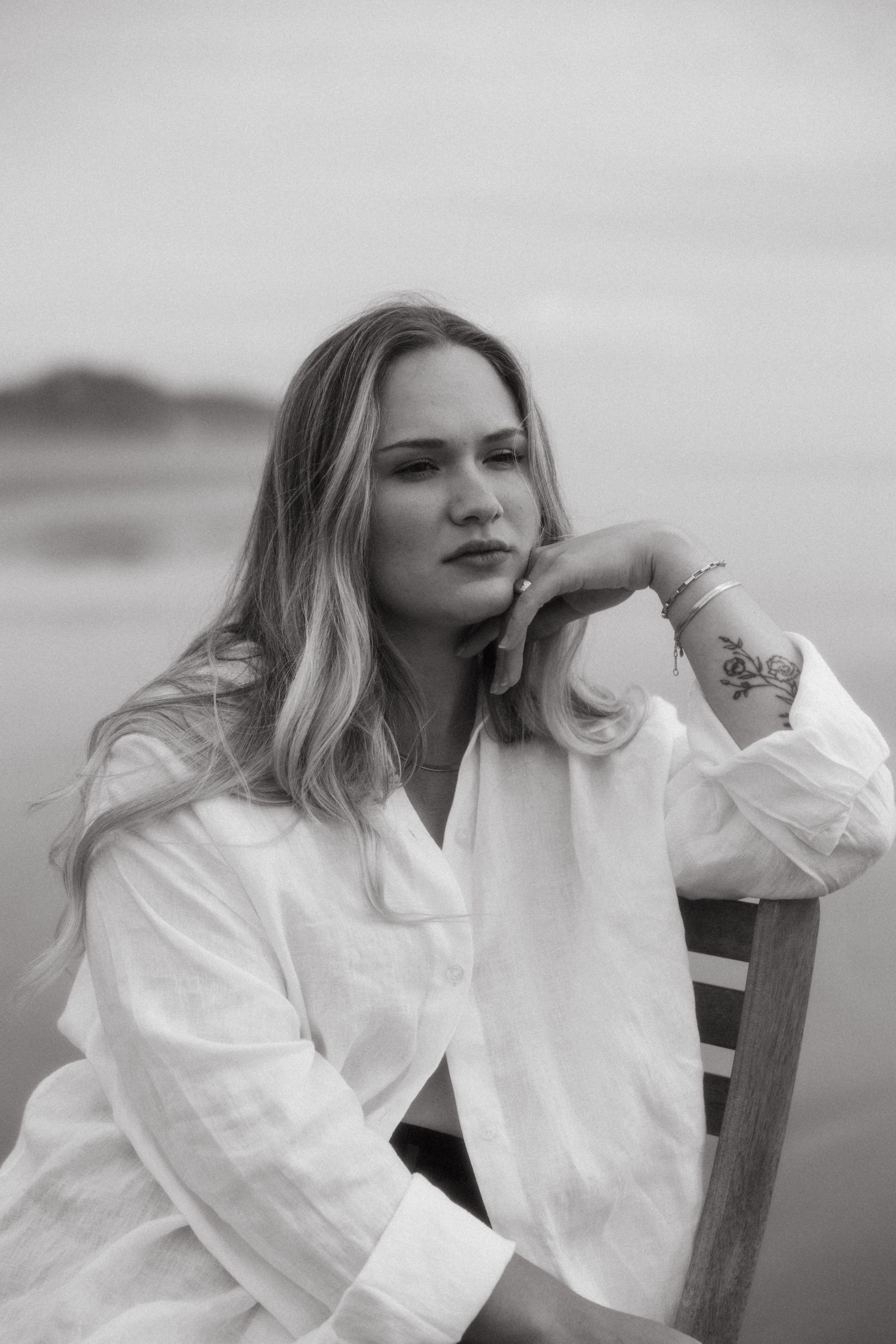 Portrait of someone in white shirt sitting by the ocean on an overcast day.