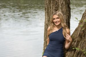 Portrait of a person in a navy dress posing by a tree near a lake.