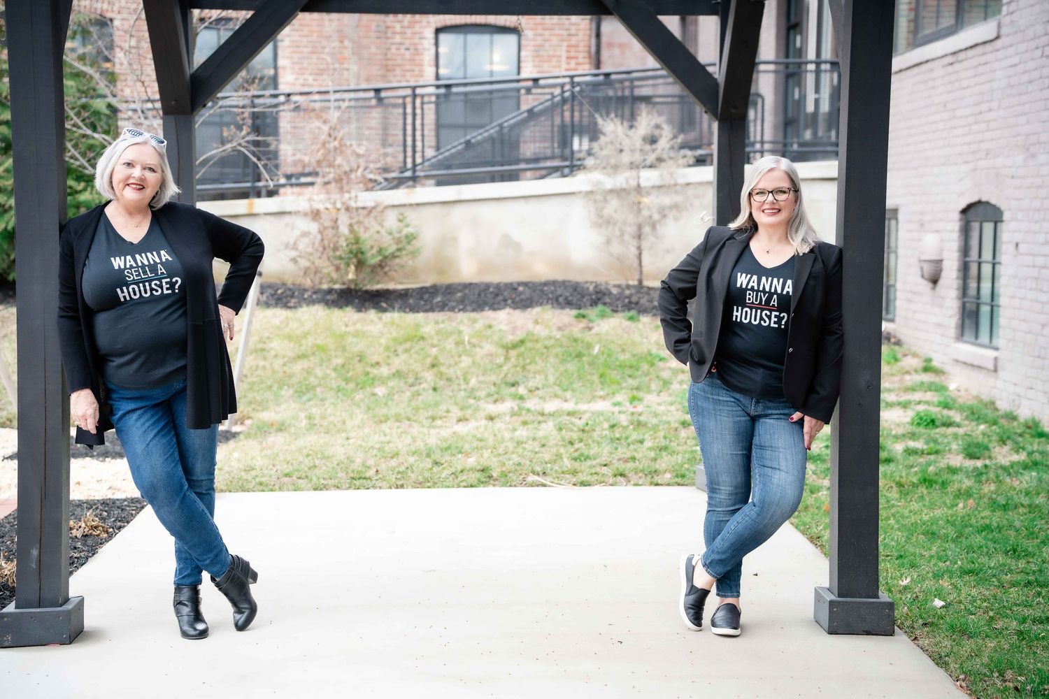 Two people in matching black sweatshirts and jeans pose casually under a covered walkway.