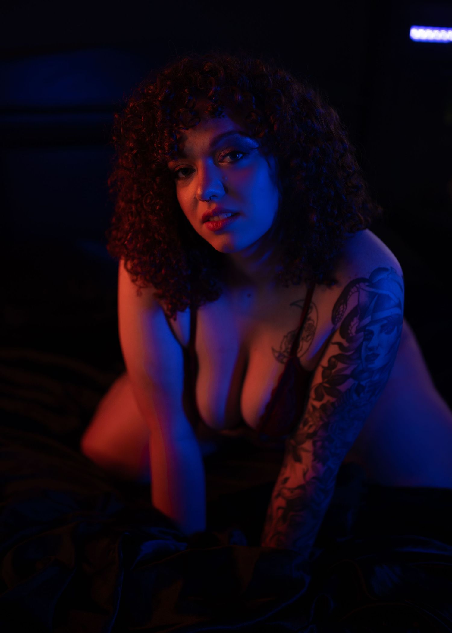 A portrait bathed in blue lighting showing tattoo art and curly hair.