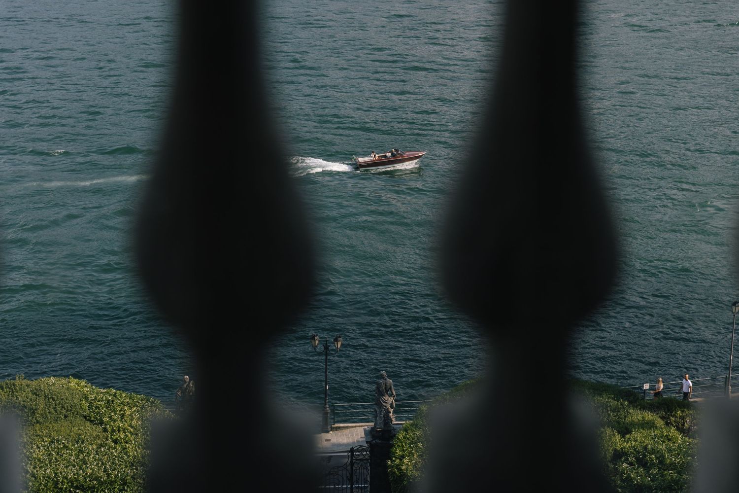 Small boat on lake seen through decorative balustrade silhouettes.