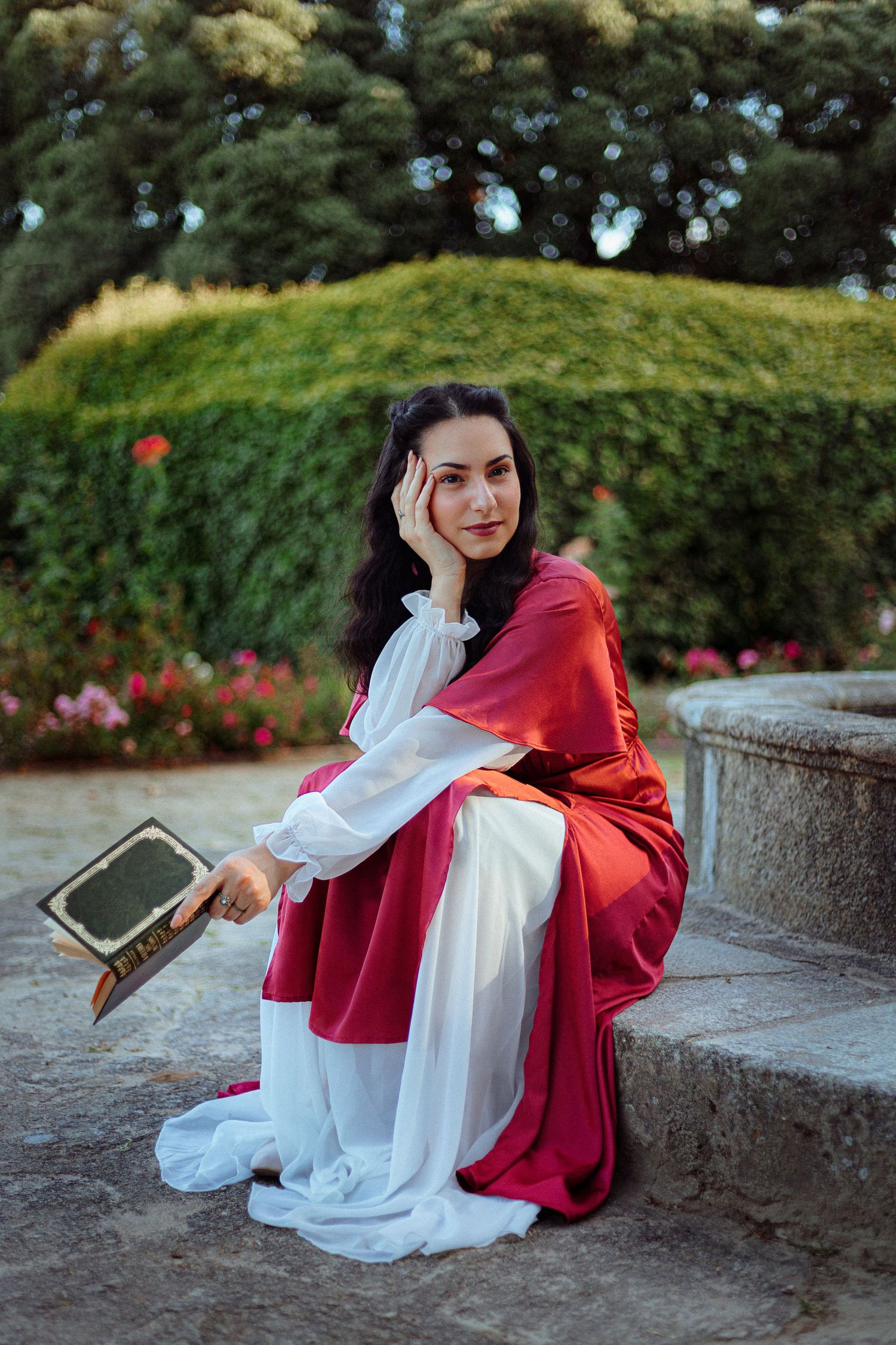 pintora do renascimento italiano rodeada de rosas num jardim vestido vermelho rosa sentada livro fonte fantasia