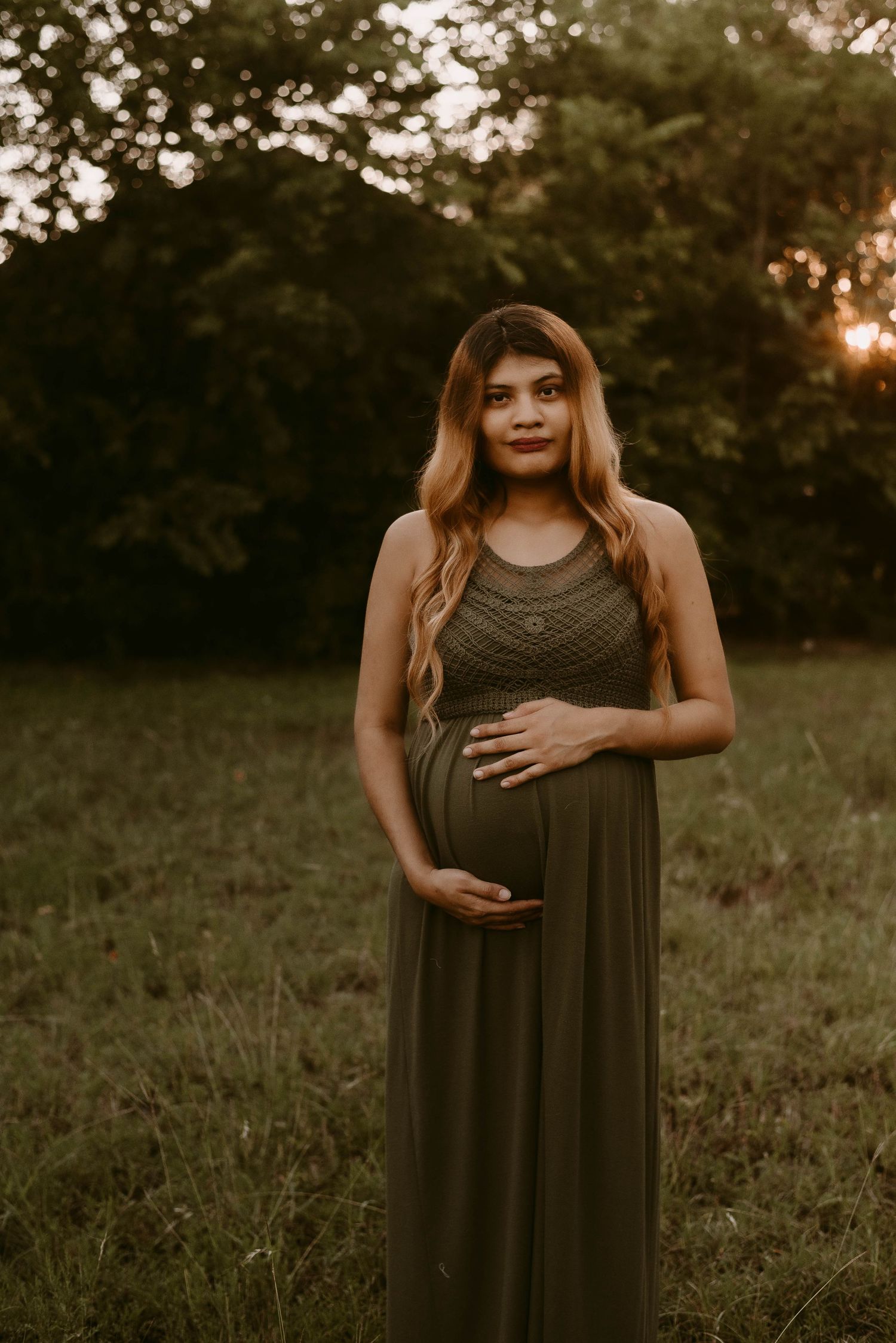 Sunset maternity photoshoot featuring olive green dress and natural outdoor backdrop.