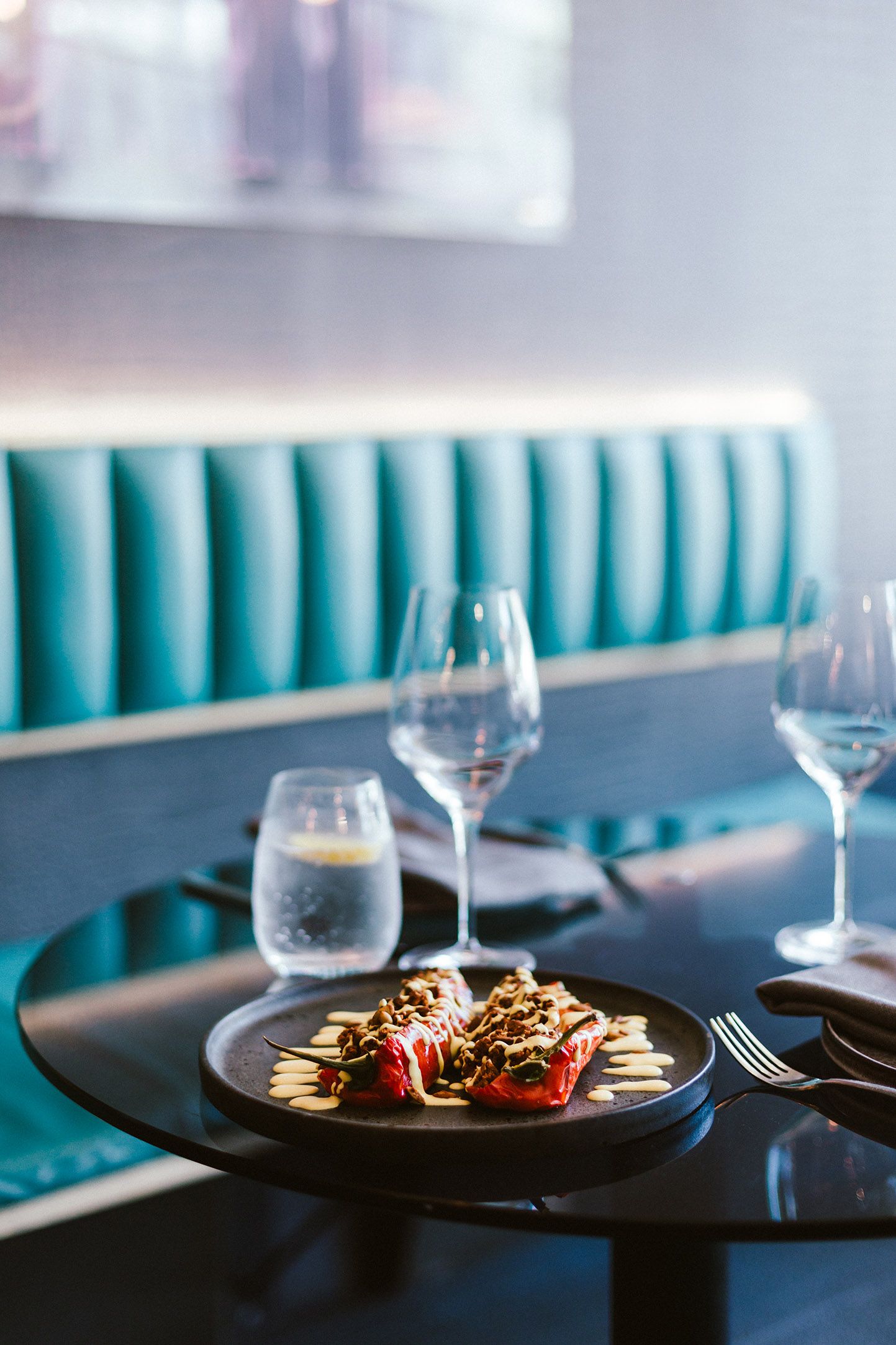 Elegant table setting with wine glasses and plates against turquoise booth seating.