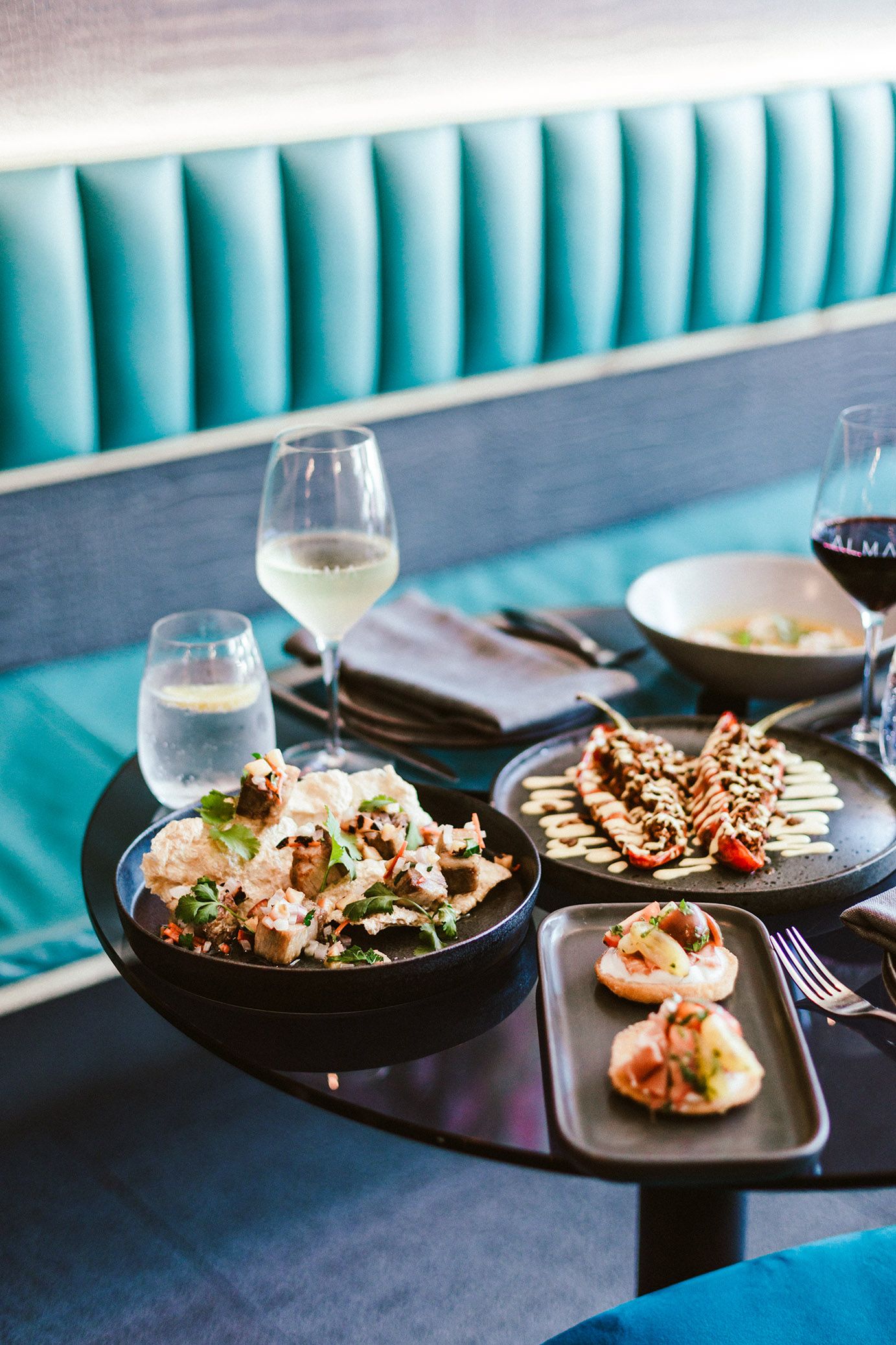 Gourmet seafood dishes served on black plates with turquoise banquette seating.