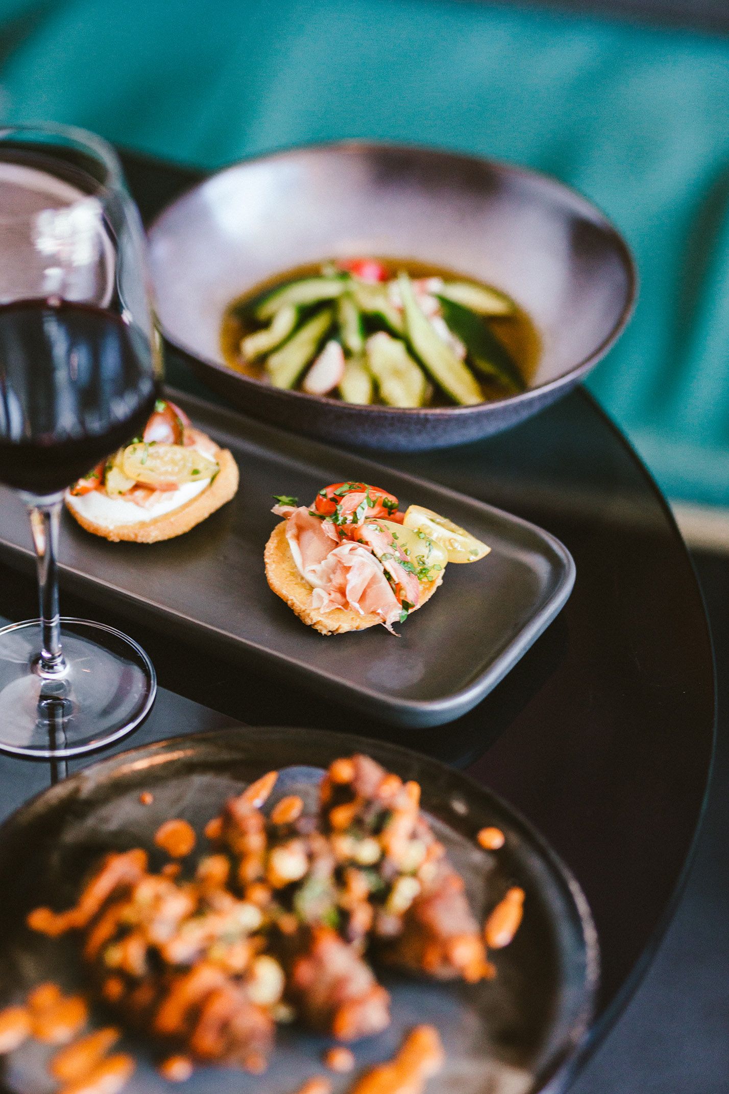 Black plates with delicate appetizers and garnishes arranged on a modern dining table.