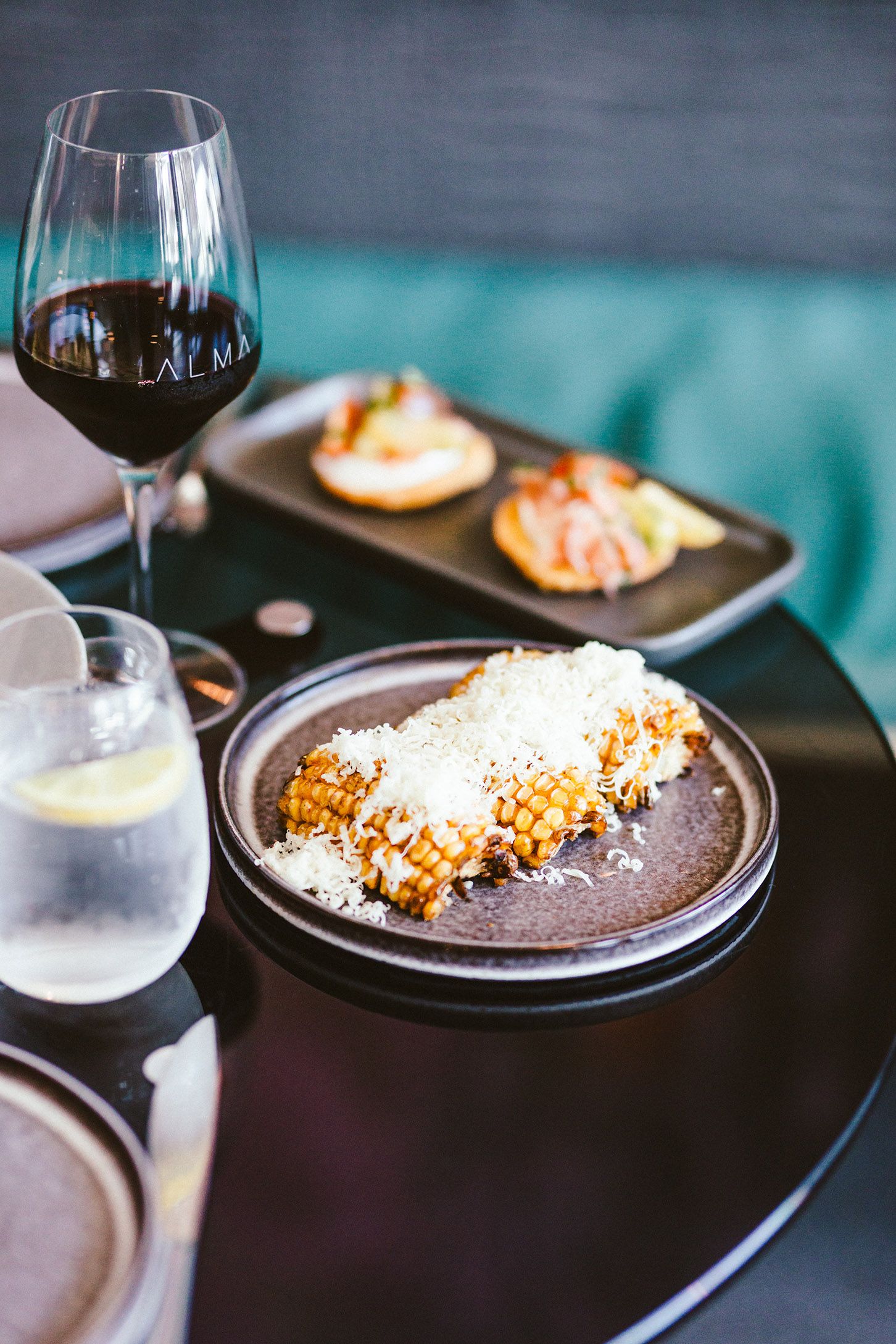 Dark plates with grated cheese garnish served alongside wine glasses in an upscale dining setting.