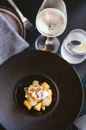 Modern black plate with cubed yellow ingredients and white garnish served with wine.